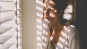 Frau blickt nachdenklich aus dem Fenster und reflektiert über ihre Selbstzweifel.