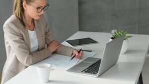 Frau sitzt nachdenklich an ihrem Schreibtisch im Büro und fragt sich, warum sie ständig Bestätigung braucht.